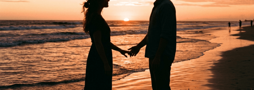 Silhouetted couple holding hands on beach at sunset