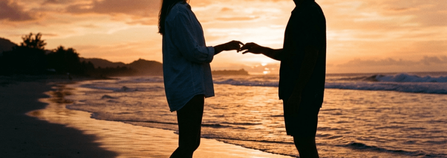 Silhouettes of a man and woman holding hands on a beach at sunset